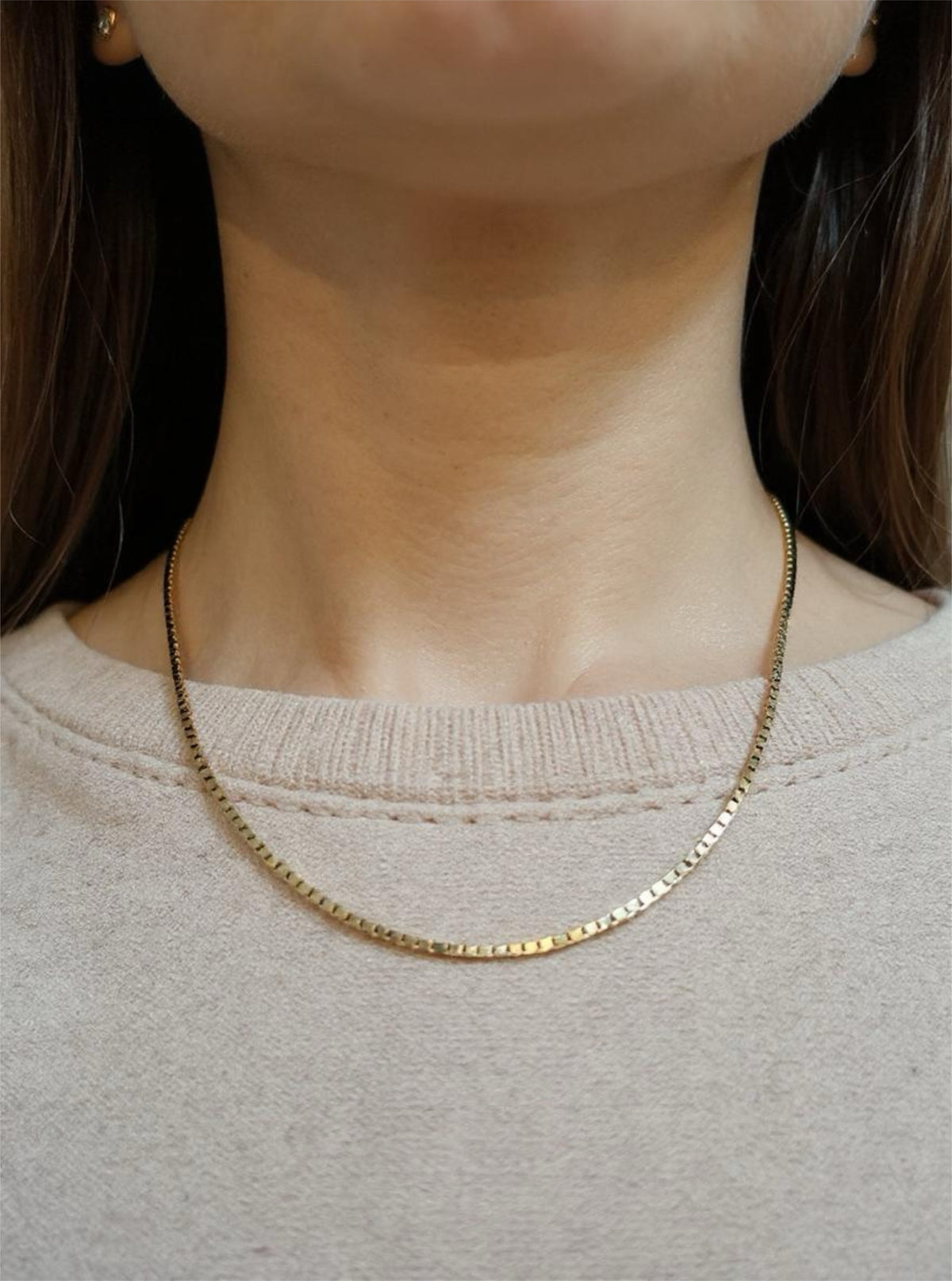 Gold necklace worn by a person with a neutral background