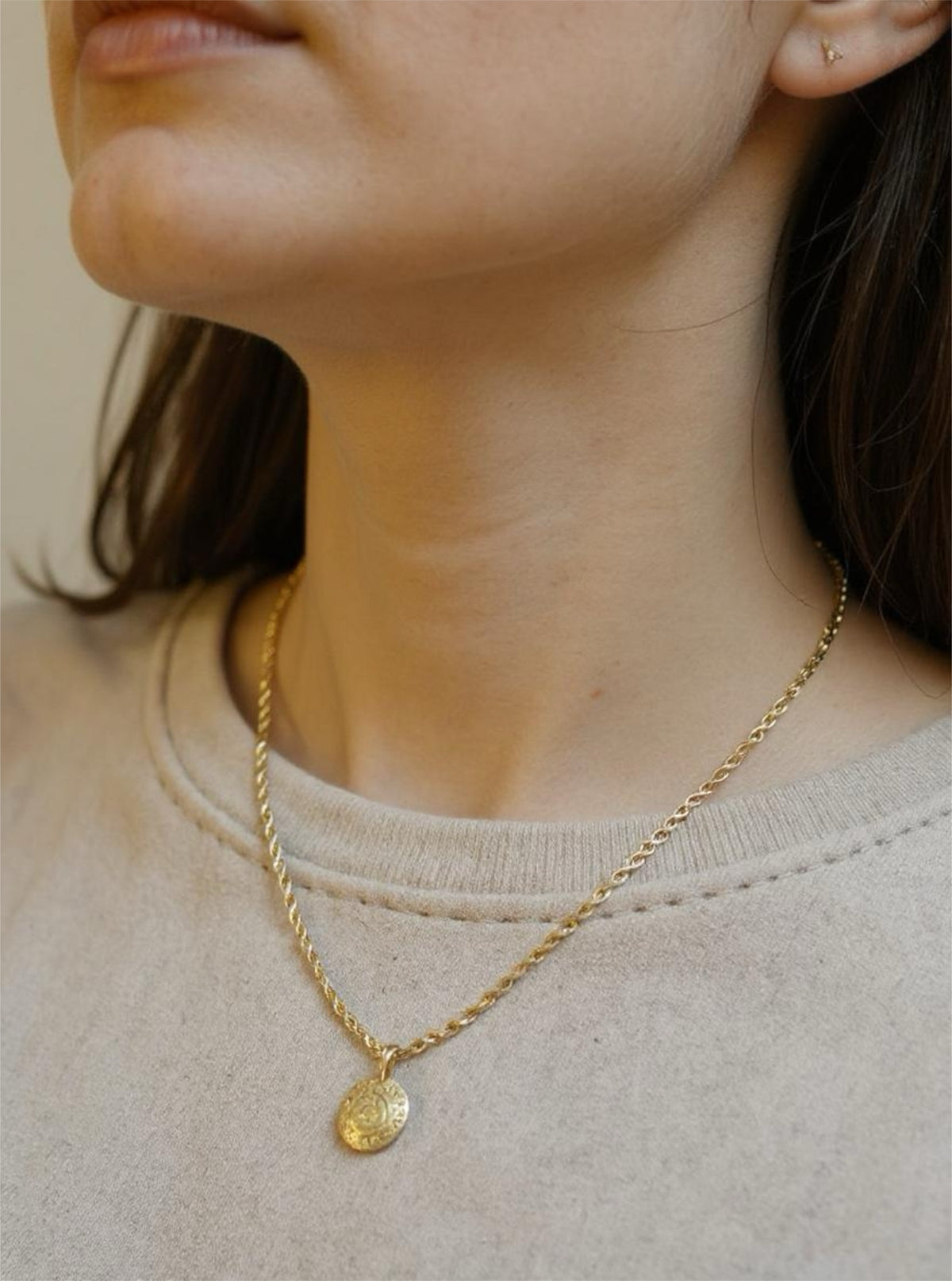 Gold necklace with a pendant worn by a person against a neutral background