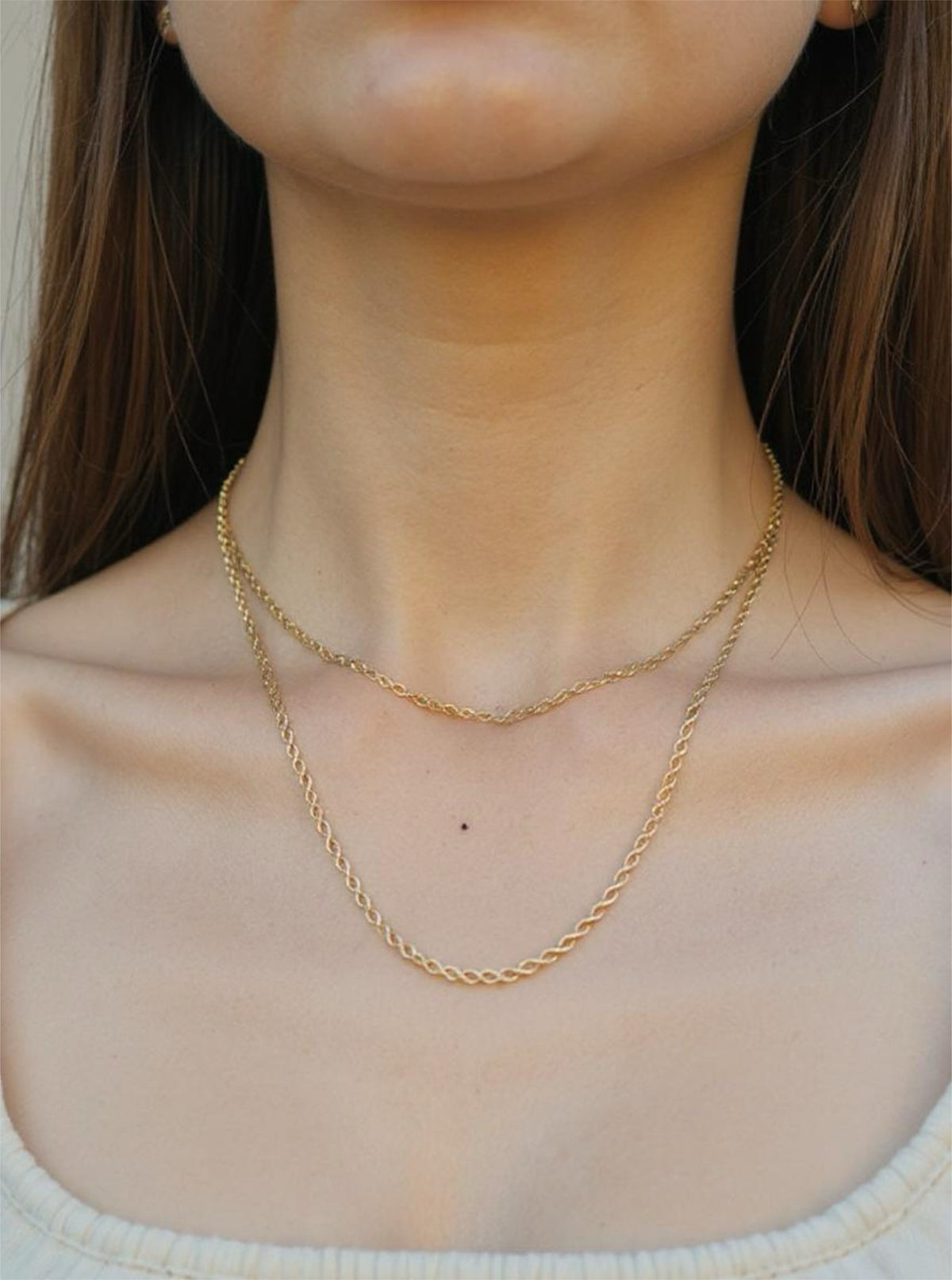 Gold chain necklace on a person with a neutral background
