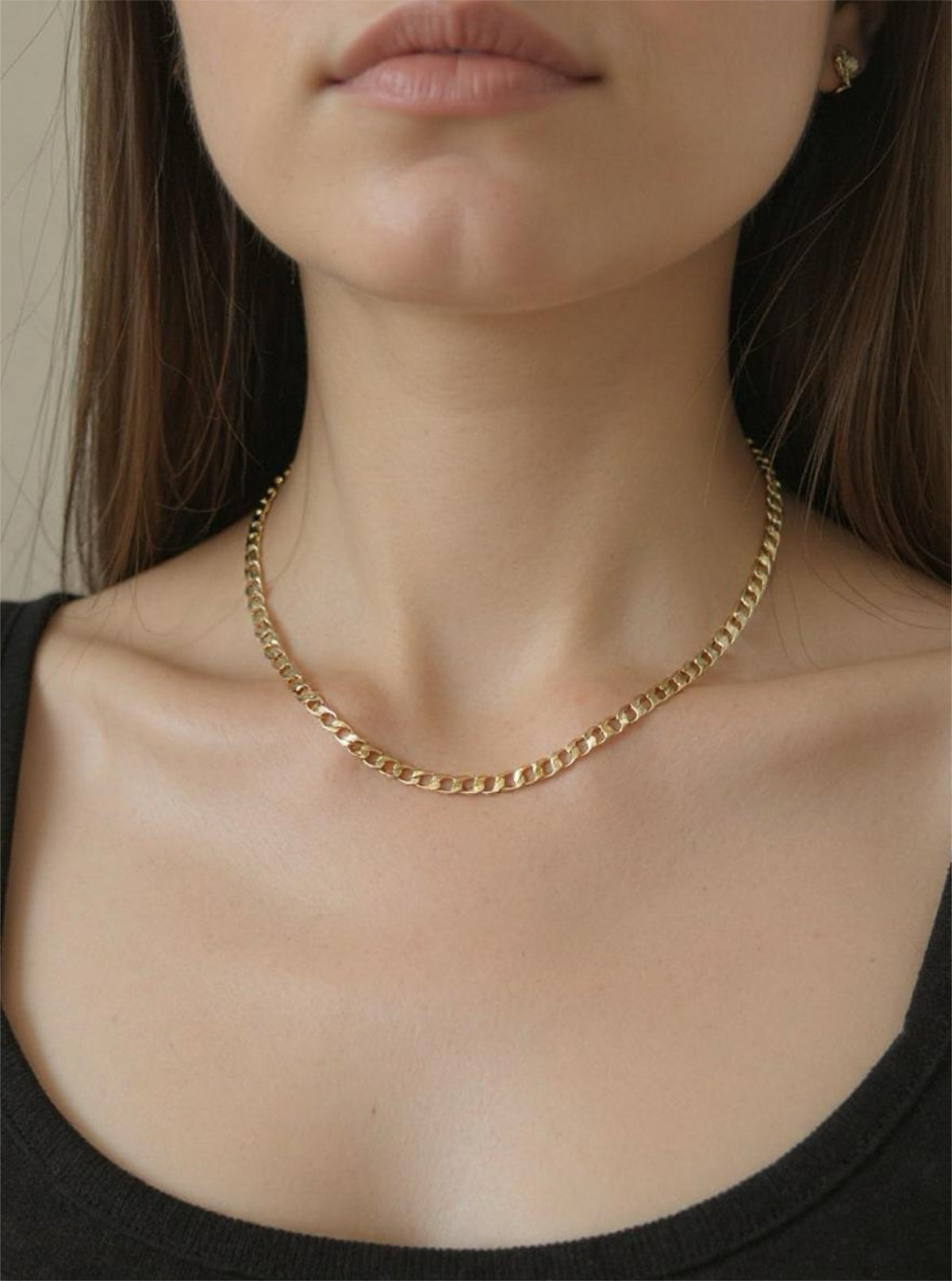 Gold chain necklace worn by a person with a neutral background