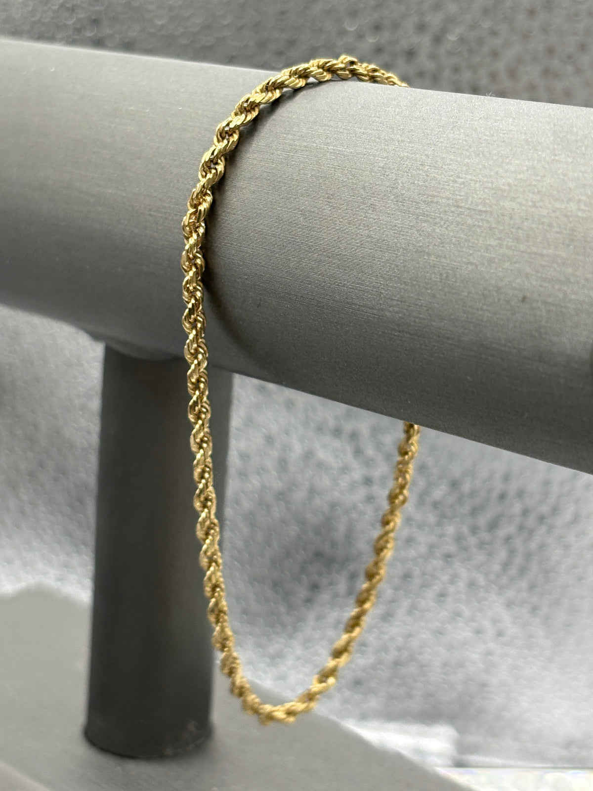Gold bracelet on a mannequin arm against a neutral background