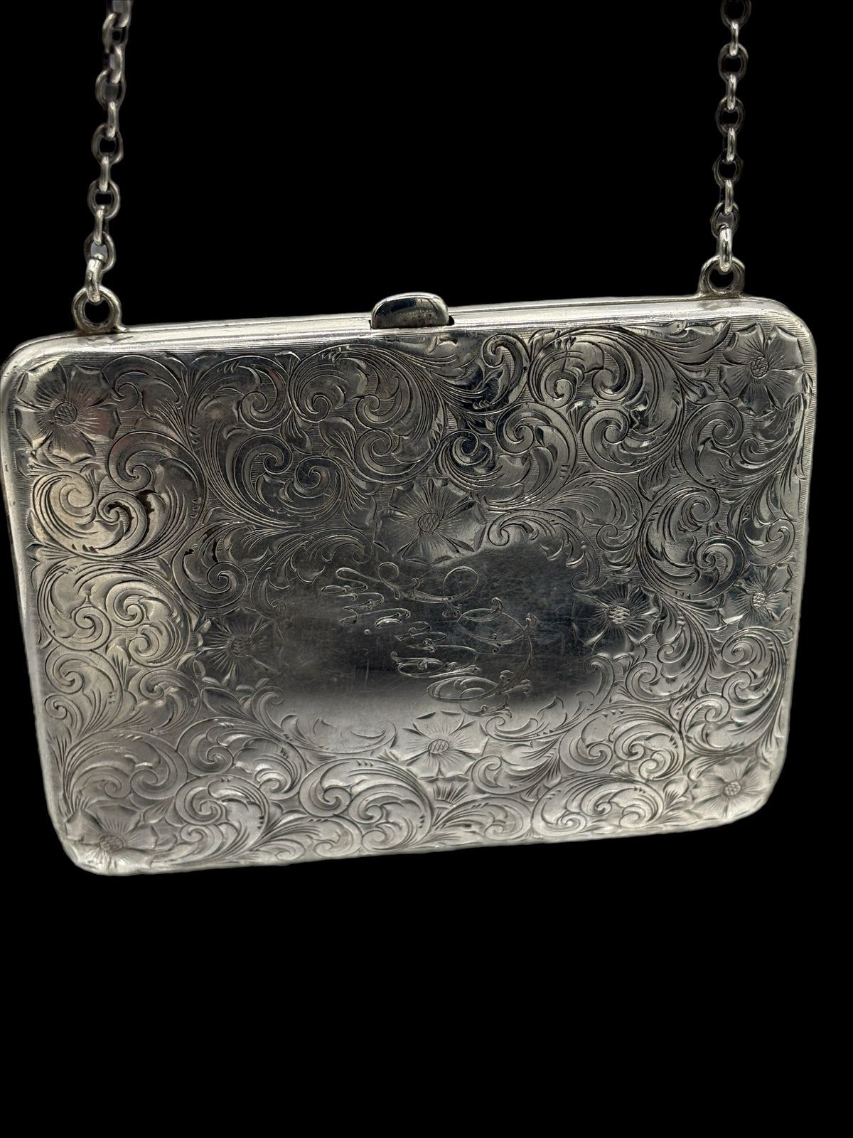 Silver embossed clutch bag with chain strap on a black background