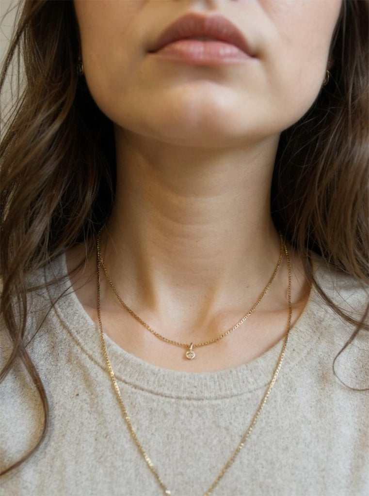 Close-up of a person wearing a delicate gold necklace with a small pendant.
