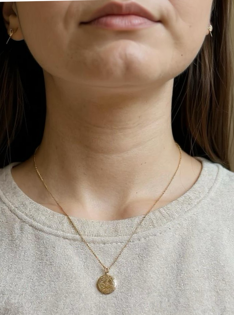 Close-up of a person wearing a gold necklace with a pendant.