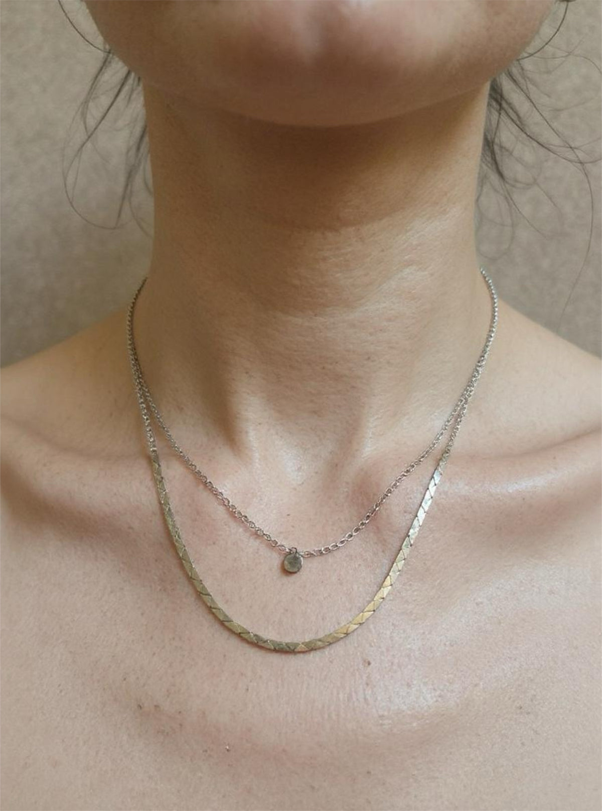 Close-up of a person wearing two necklaces on a neutral background