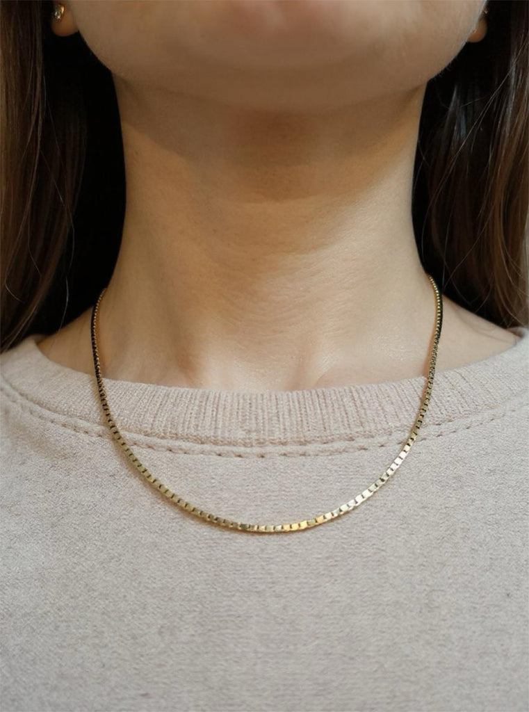 Gold necklace worn by a person with a neutral background