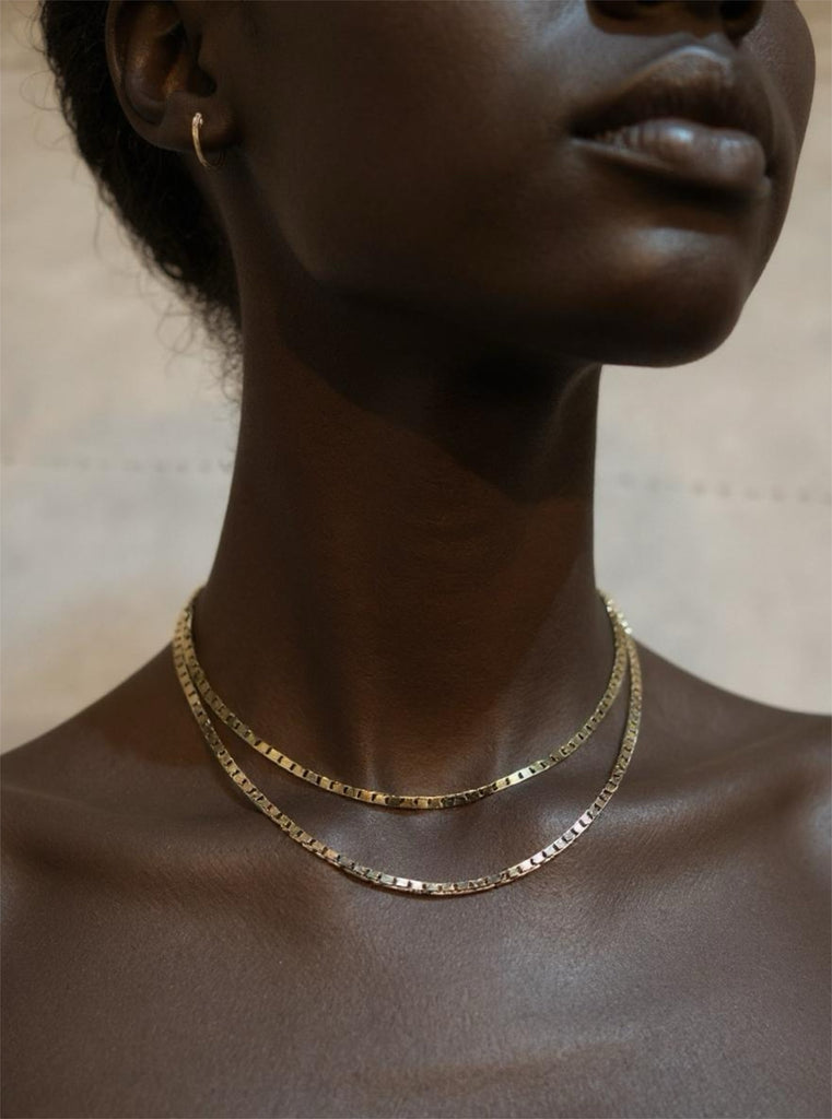 Close-up of a person wearing a gold necklace with a neutral background