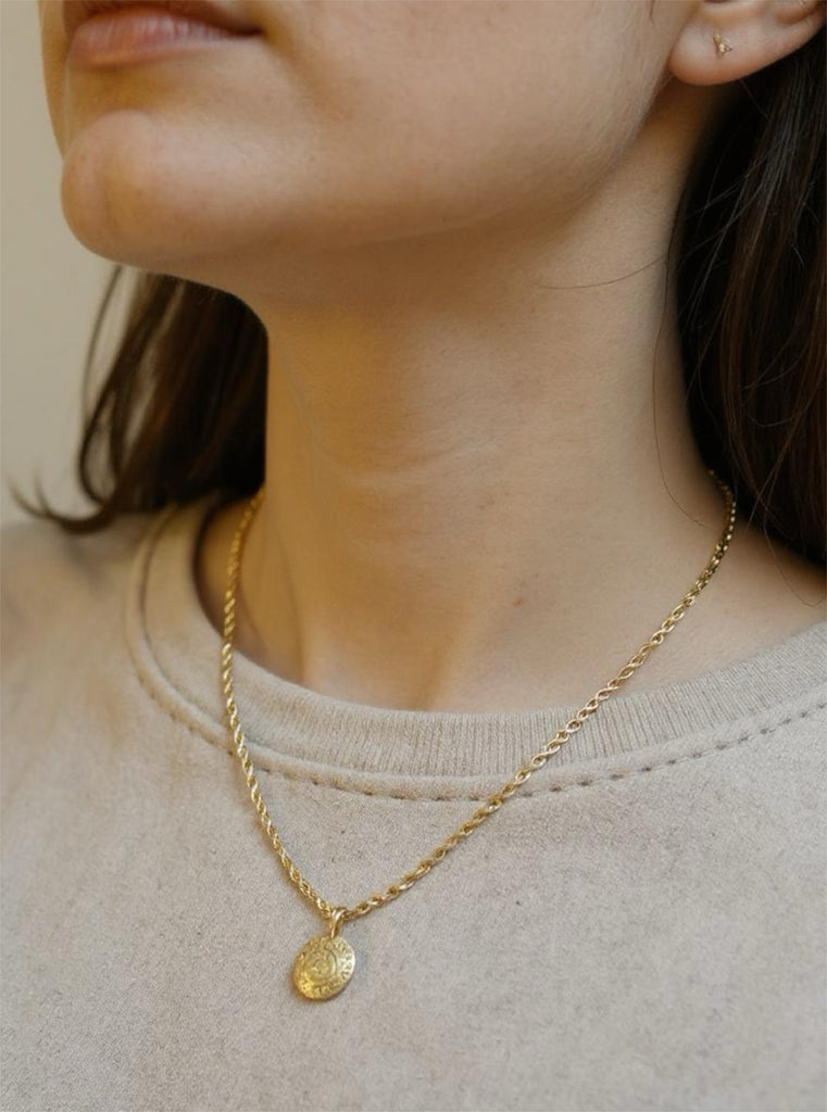 Gold necklace with a pendant worn by a person against a neutral background