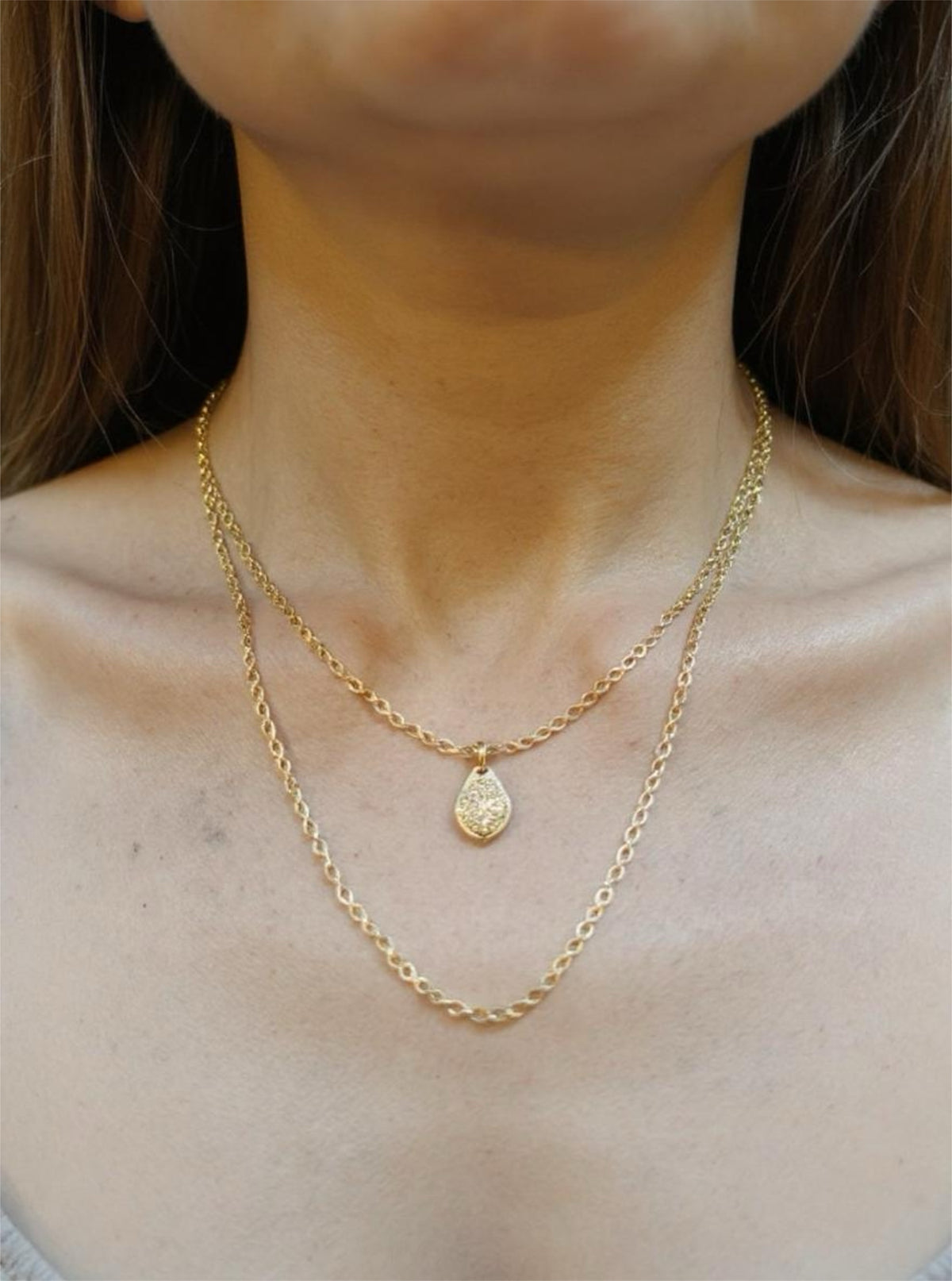 Close-up of a person wearing two gold necklaces with a pendant.