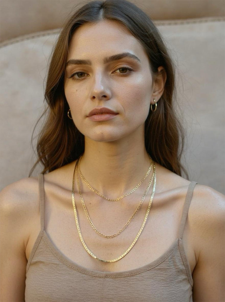 Woman wearing gold necklaces and earrings against a neutral background