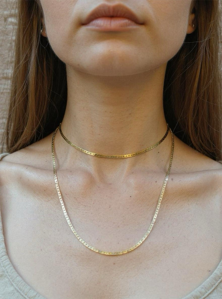 Gold necklace worn by a person with a neutral background