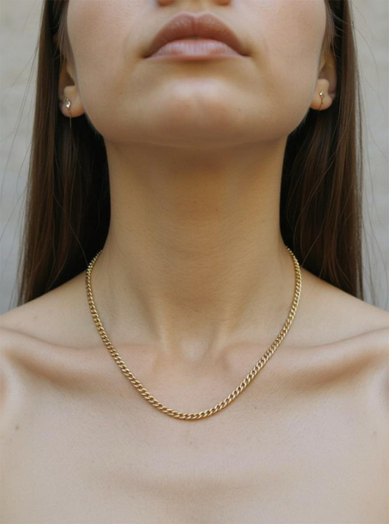 Gold chain necklace worn by a person with a neutral background