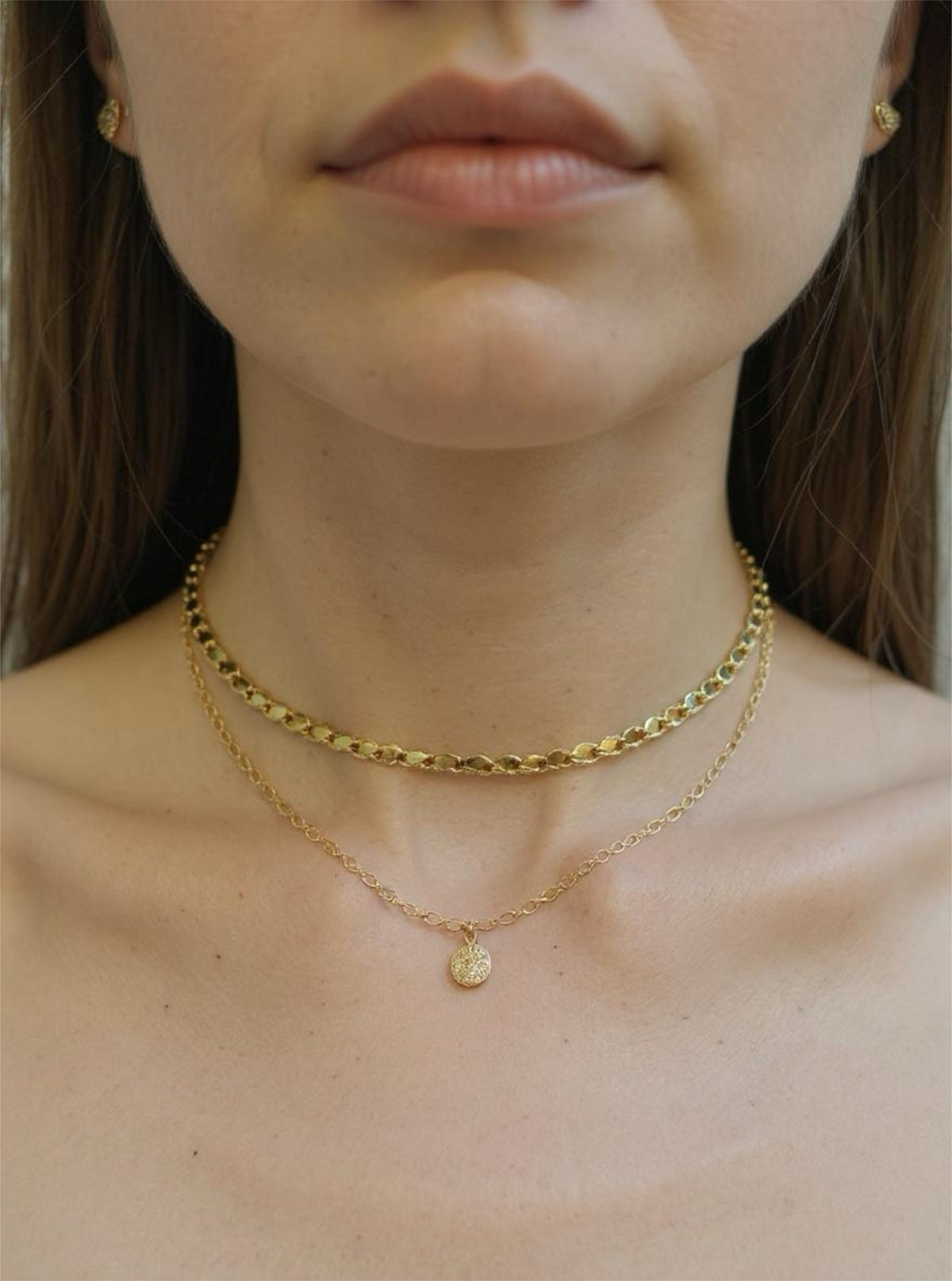 Close-up of a person wearing two gold necklaces with a plain background