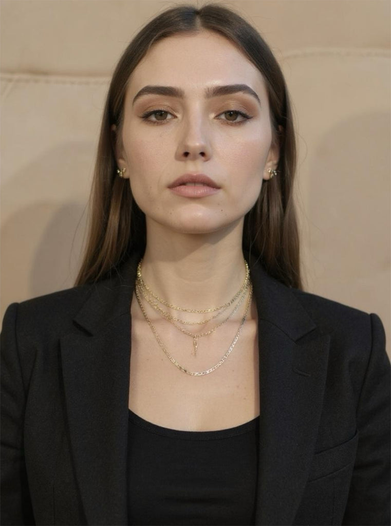 Woman wearing a black blazer and layered gold necklaces against a neutral background