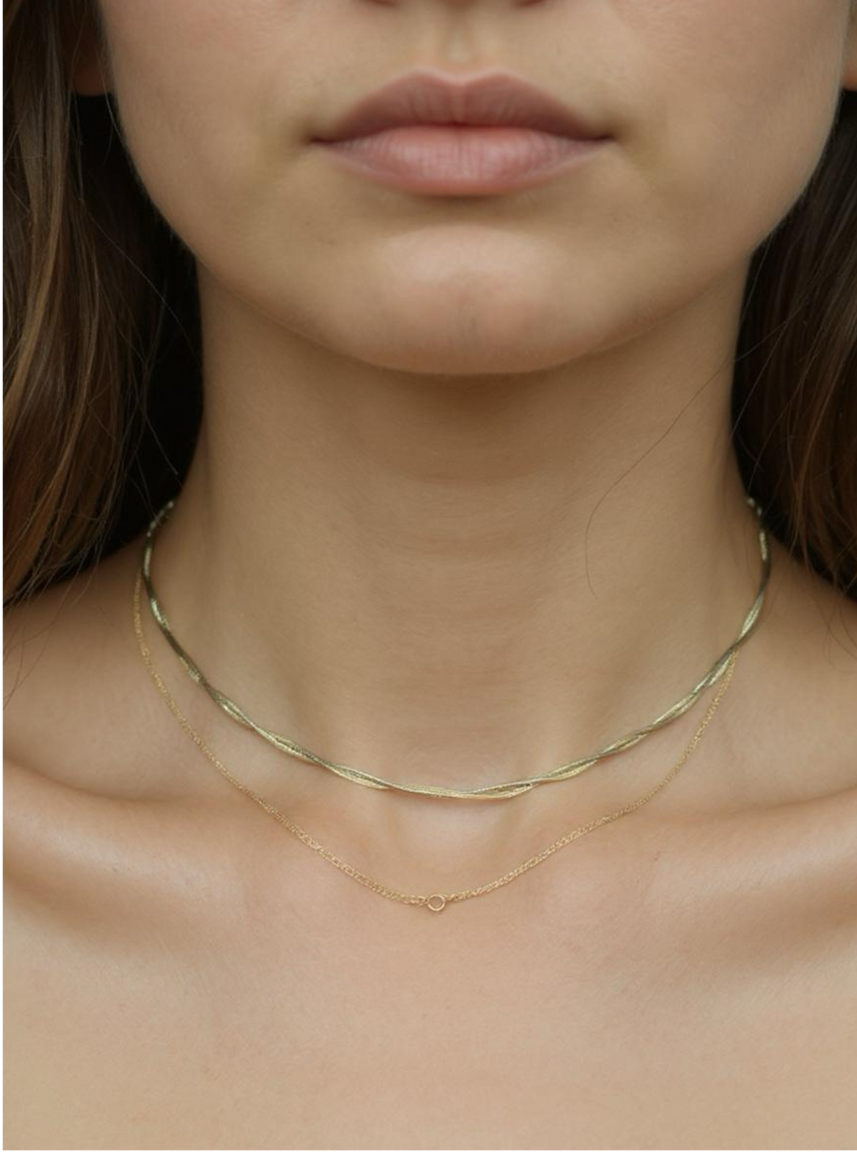 Close-up of a person wearing two gold necklaces on a plain background